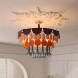 Illuminated multicolor chandelier hangs beneath an ornate white ceiling rose in a room with paneled walls and an arched opening.