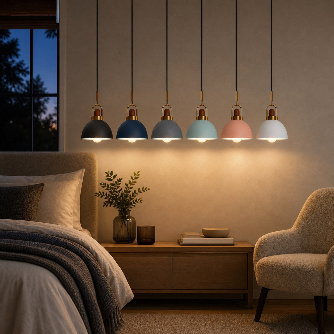 Five modern pendant lights with dome-shaped shades in dark blue, light blue, and soft pink, hanging in a row above a bed in a cozy, warmly lit bedroom.