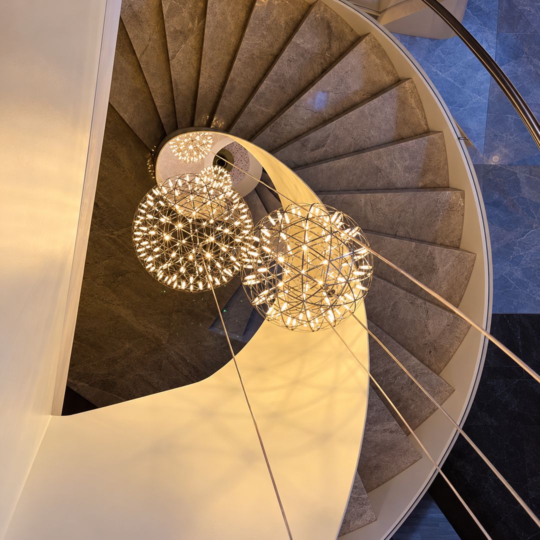 Globe pendant light grouping with illuminated metal lattice frames hangs through the center of a curved staircase.