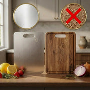 Two rectangular cutting boards with cutout handles are shown on a kitchen counter: one brushed stainless steel and one natural wood, with food items around them. Two circular callout graphics at the top show a mirror on the plain board and a close-up of wood shavings crossed out, suggesting the board is self-cleaning or resistant to staining.
