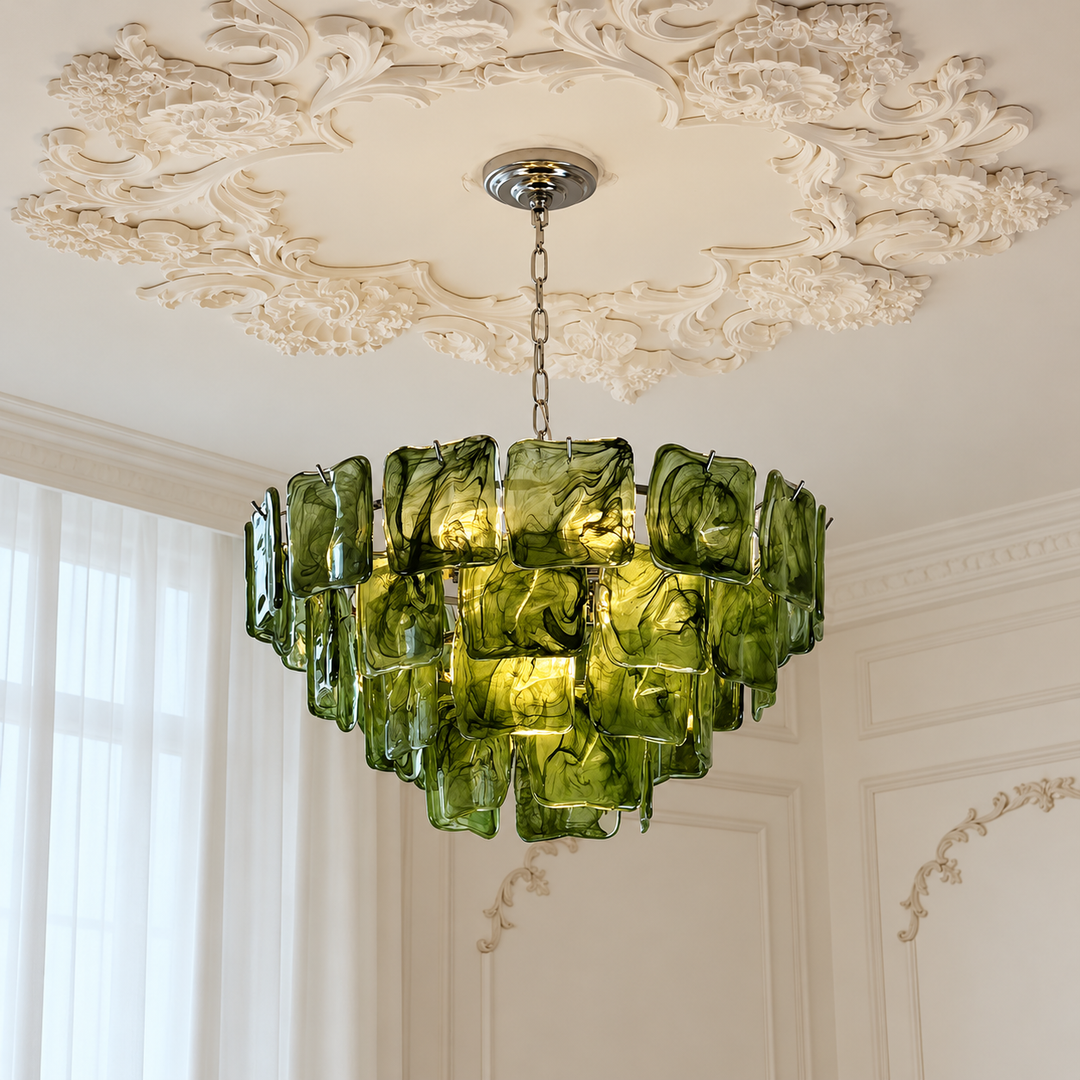 A modern chandelier with multiple overlapping translucent green glass shades hanging from a silver chain in an ornate cream-colored room with decorative ceiling moldings.