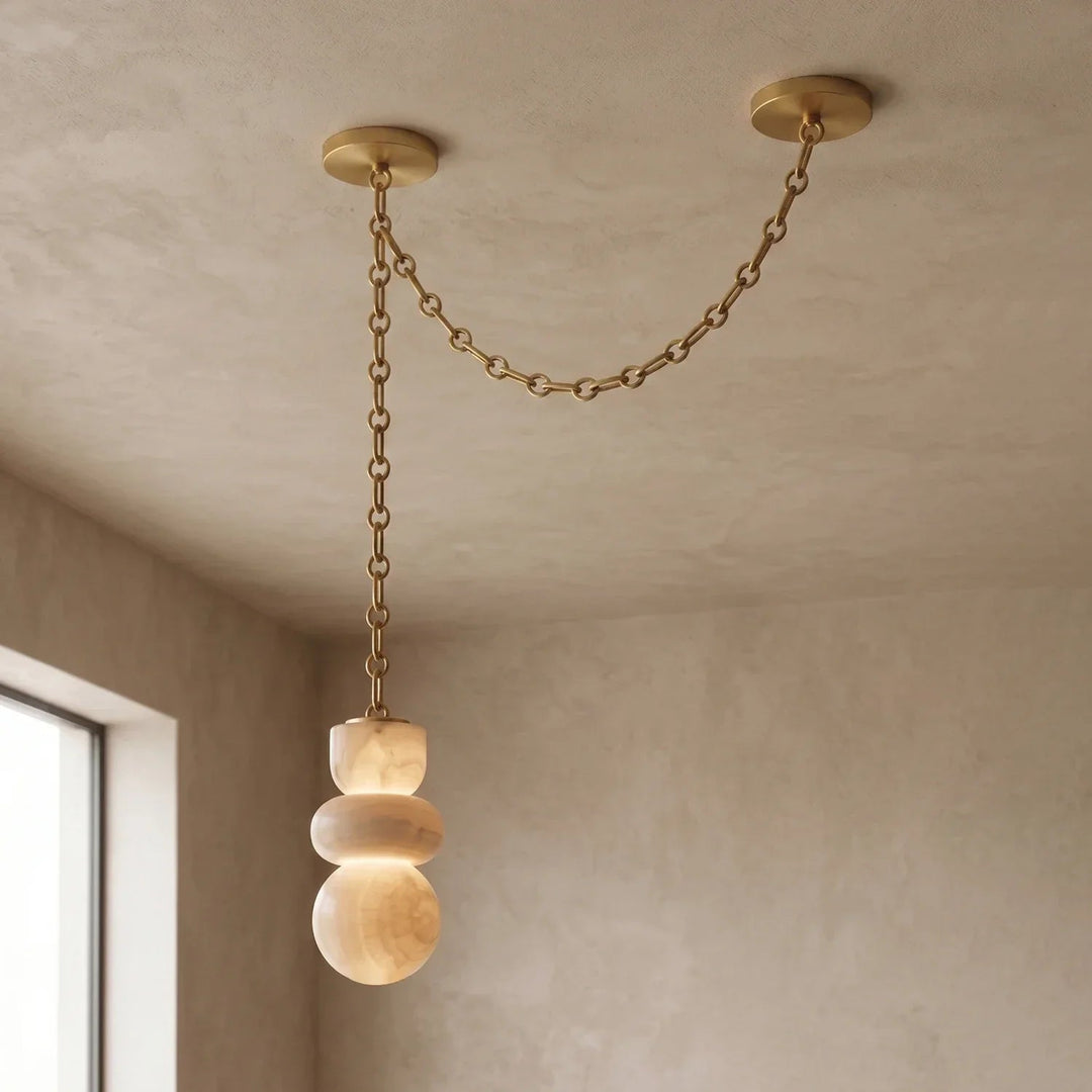 An alabaster chandelier hangs beside a window, with a gold-toned chain draped between two ceiling mounts.
