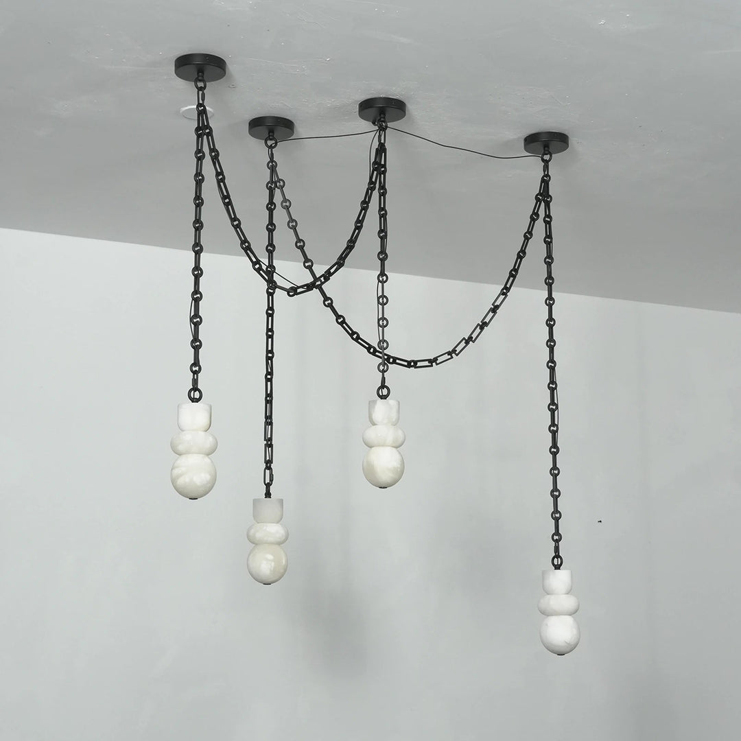 Angled view of an unlit chandelier with four white alabaster shades hanging at different heights from black chains against pale walls.
