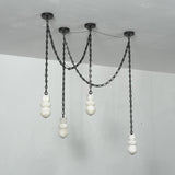 Angled view of an unlit chandelier with four white alabaster shades hanging at different heights from black chains against pale walls.