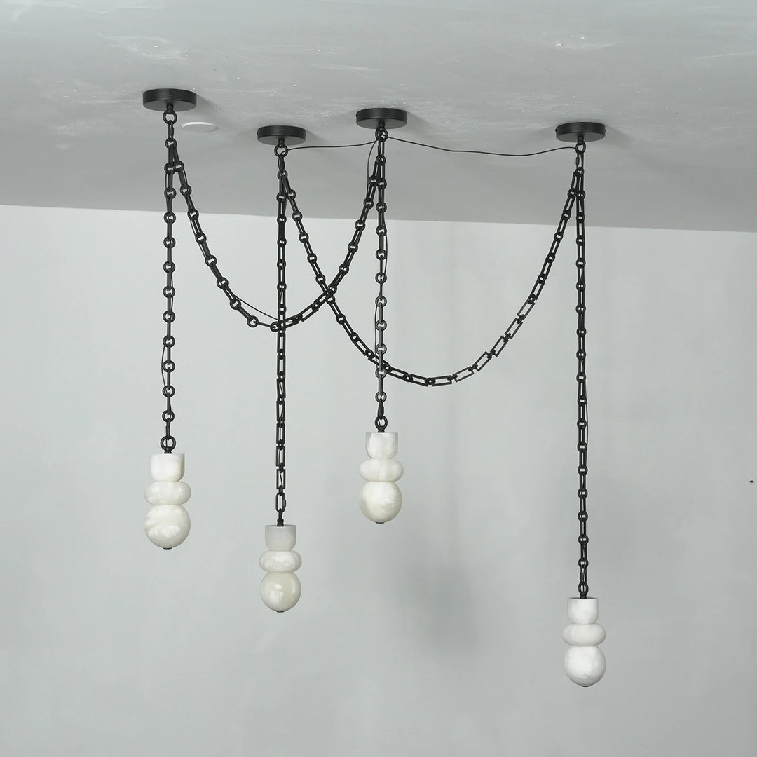Front view of an unlit chandelier with four sculpted white alabaster shades, draped black chains, and round black ceiling mounts.