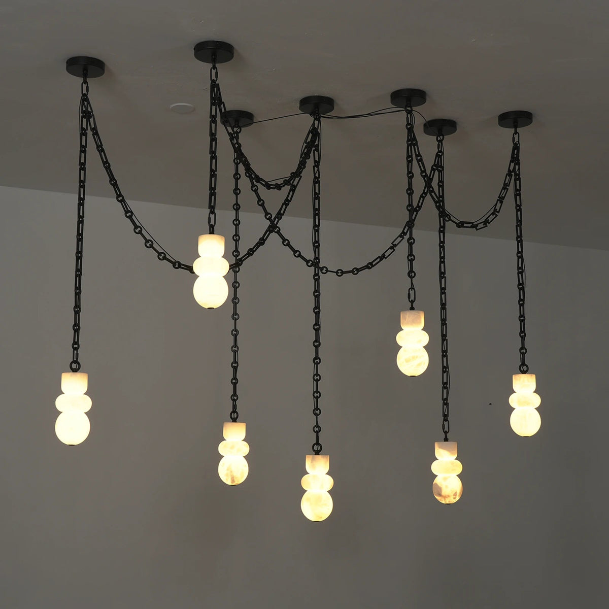 A modern industrial-style chandelier with multiple black chain drops and stacked frosted glass bulbs, shown illuminated against a plain ceiling.