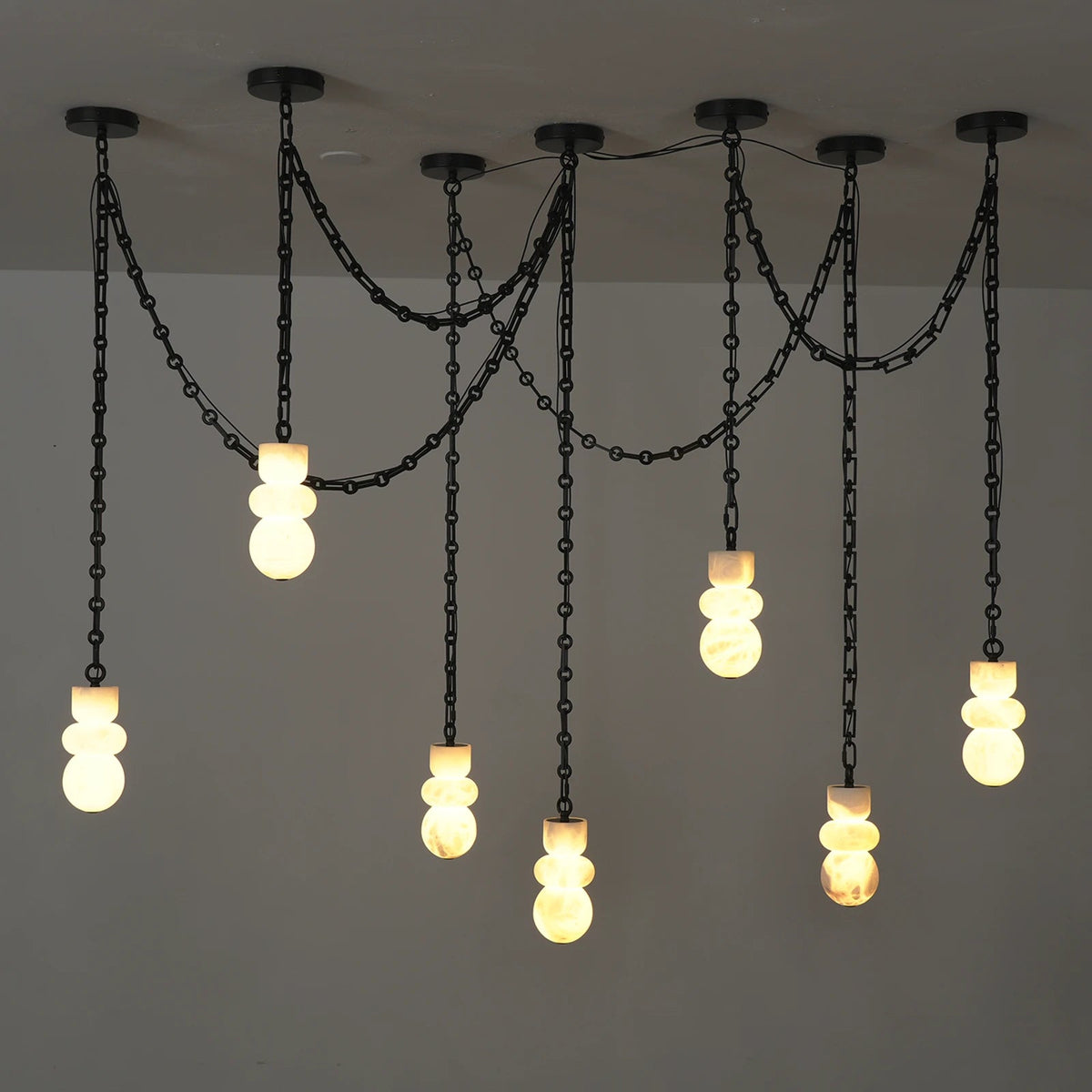 A multi-light pendant chandelier with black metal chains and spherical glass shades, shown hanging against a plain light gray wall.