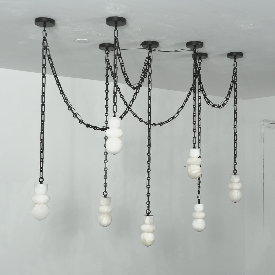 A modern multi-light chandelier with black metal chains and spherical white glass shades, suspended from a ceiling in a minimalist room.