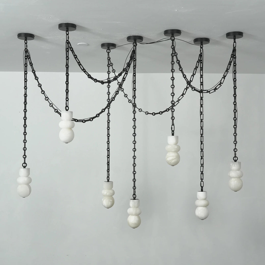 A modern multi-light linear chandelier with black metal chains and spherical white glass shades, suspended from a ceiling against a plain light gray wall.