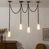 An illuminated alabaster chandelier with four sculpted shades hangs from draped black chains against a white wall above wooden furniture.