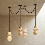 Alabaster chandelier with four glowing stone drops at staggered heights and black chains against textured cream walls.