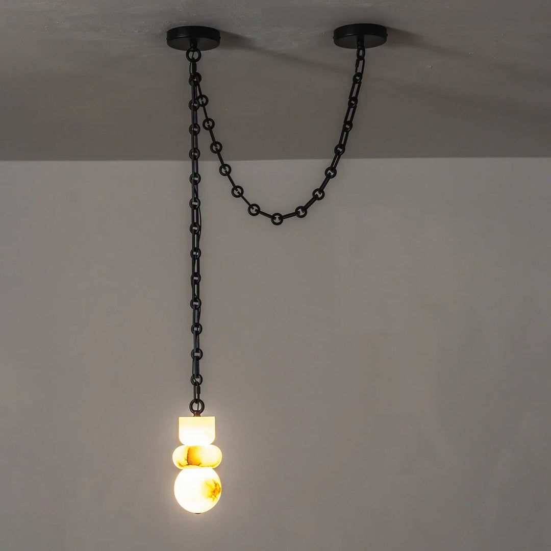 Glowing alabaster chandelier hangs from a black chain draped between two round ceiling mounts against a gray wall.