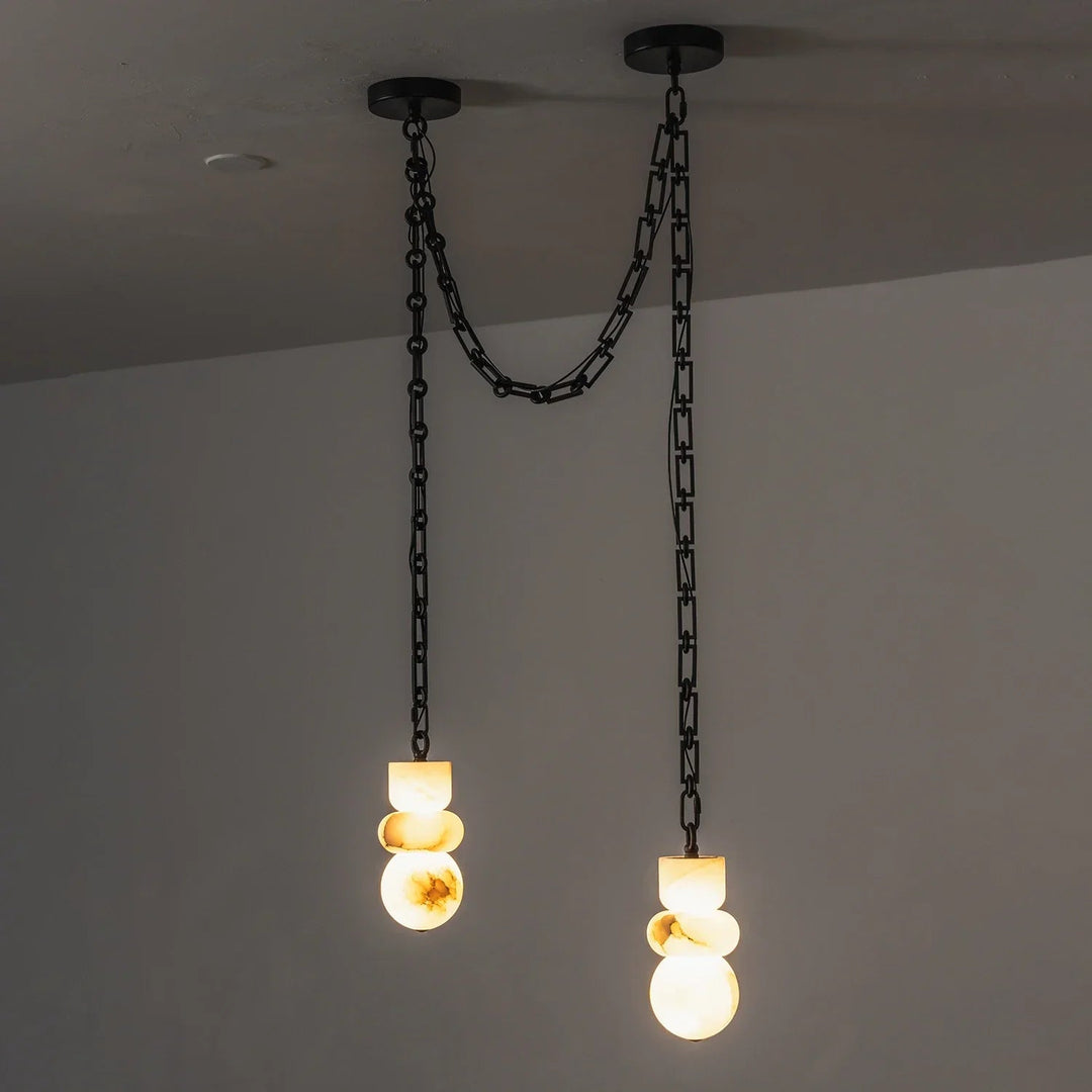 Alabaster chandelier has two glowing drops at different heights, suspended from black chains against a gray wall.