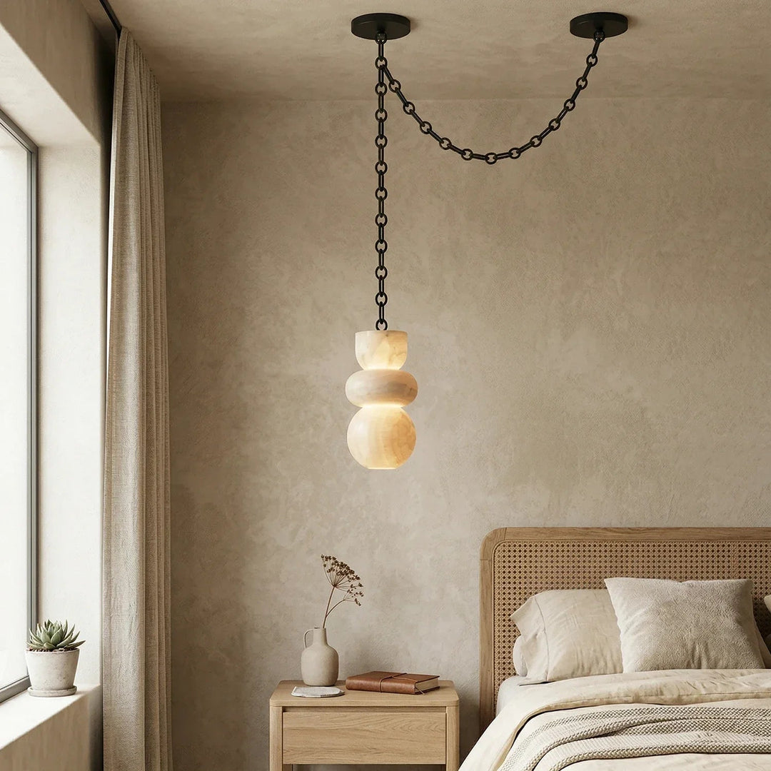 A cream alabaster chandelier hangs from a draped black chain above a wooden nightstand beside a woven headboard.