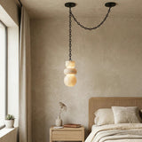 A cream alabaster chandelier hangs from a draped black chain above a wooden nightstand beside a woven headboard.