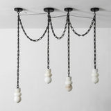 Unlit four-light alabaster chandelier with white sculpted stone shades and three black chain swags against a pale wall.