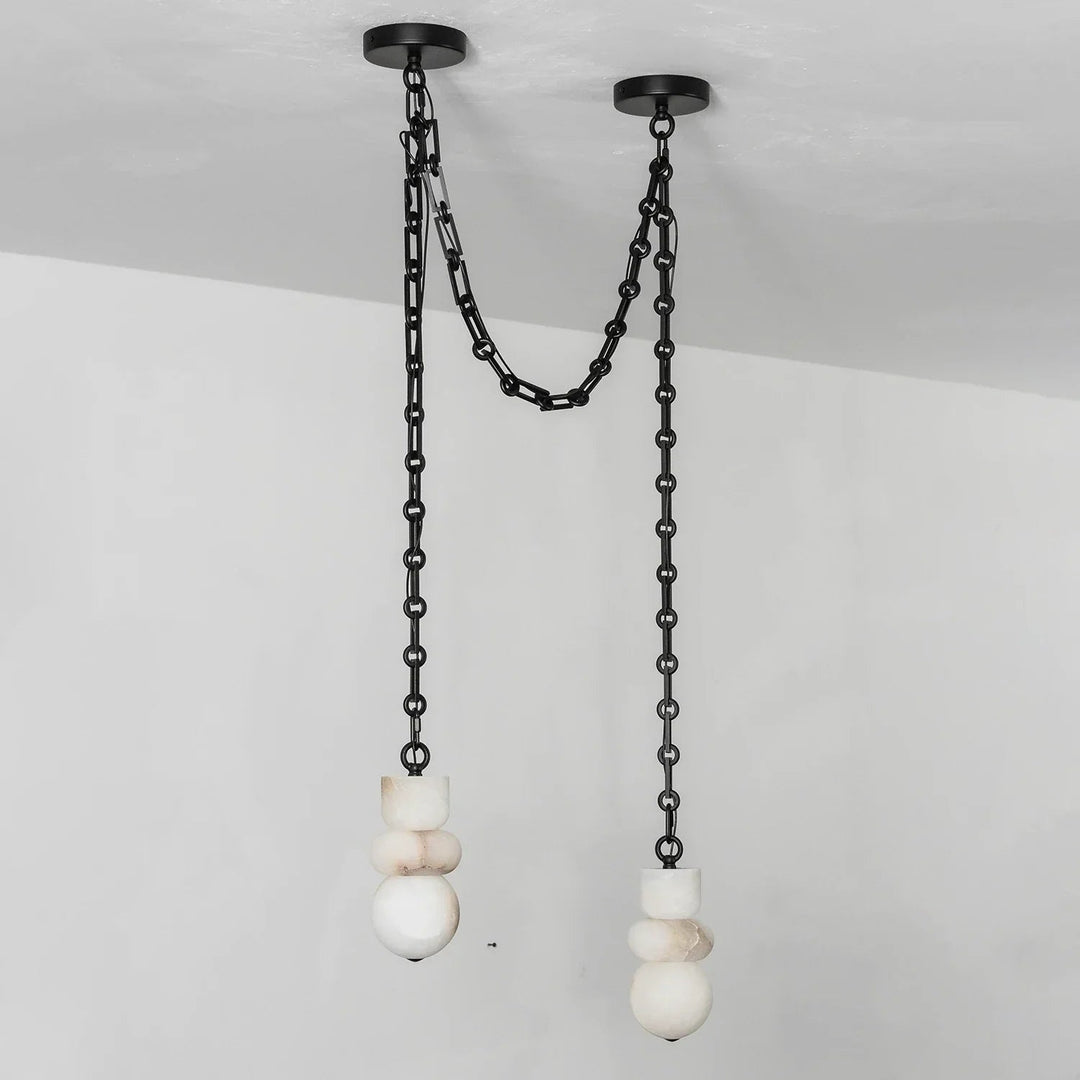 Alabaster chandelier with two white sculpted shades hanging at different heights from black swag chains against a pale wall.