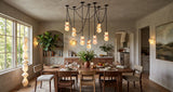 A modern multi-light pendant chandelier with multiple black metal chains and glowing frosted glass globes, hanging over a wooden dining table in a beautifully styled, warm-toned dining room.