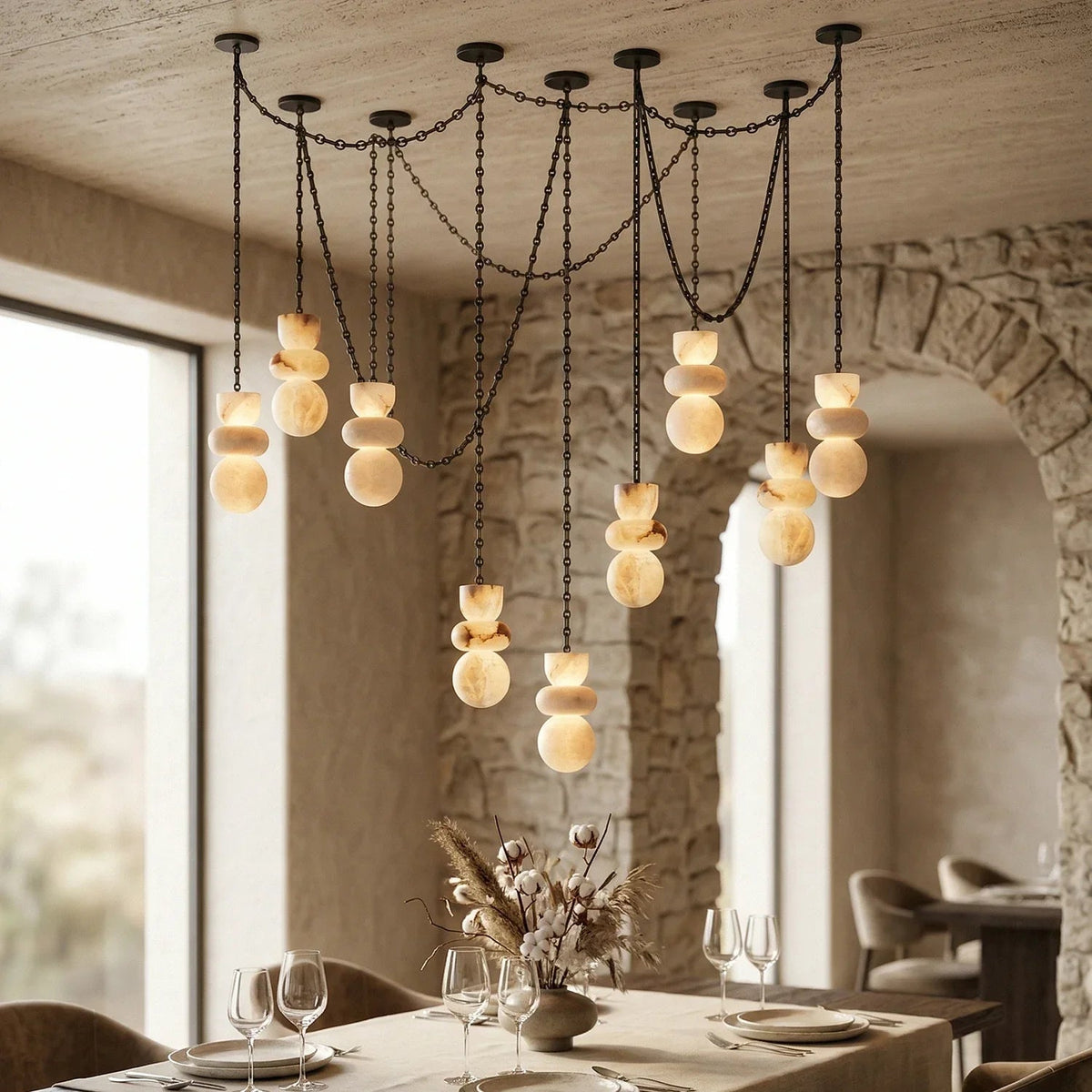 A modern chandelier with multiple black metal chains and spherical amber glass shades, hanging over a dining table in a rustic stone and wood dining room.