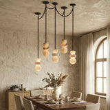 A modern multi-light pendant chandelier with stacked organic-shaped frosted glass shades hanging from a black metal frame in a rustic dining room.