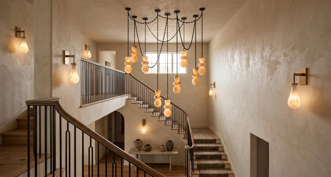 A modern multi-light chandelier with hanging glass globes and several wall sconces illuminate a staircase in a textured beige interior.