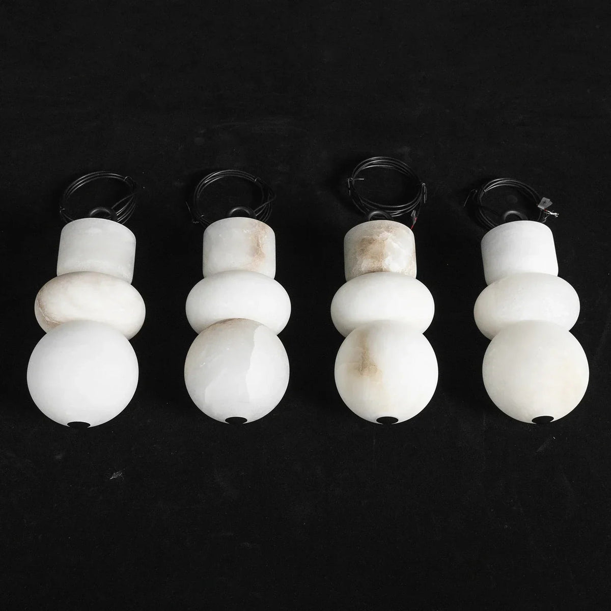 Four alabaster chandelier shades with natural cream veining stand upright against a black background.