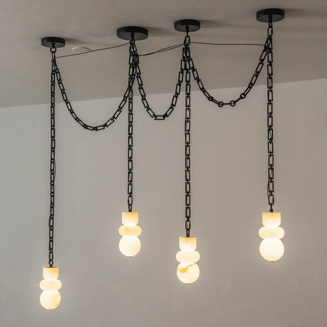 Alabaster chandelier viewed at an angle, with four glowing cream stone shades suspended from black swag chains against a gray wall.