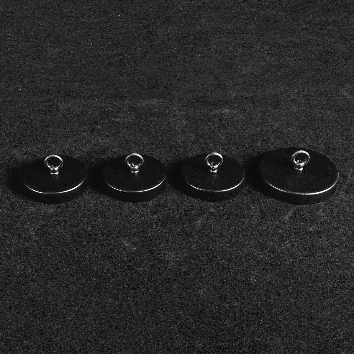 Four black round ceiling mounts in graduated sizes with metal loops for the alabaster chandelier, on a dark background.