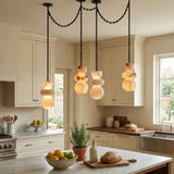An alabaster chandelier with four glowing cream stone drops hangs from black chains above a kitchen island.