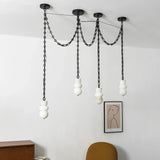 An unlit alabaster chandelier with four white sculpted shades and black chains hangs near a framed portrait and mustard chair.