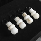 White alabaster chandelier shades in stacked sphere and cylinder shapes with coiled black cords on a dark surface.