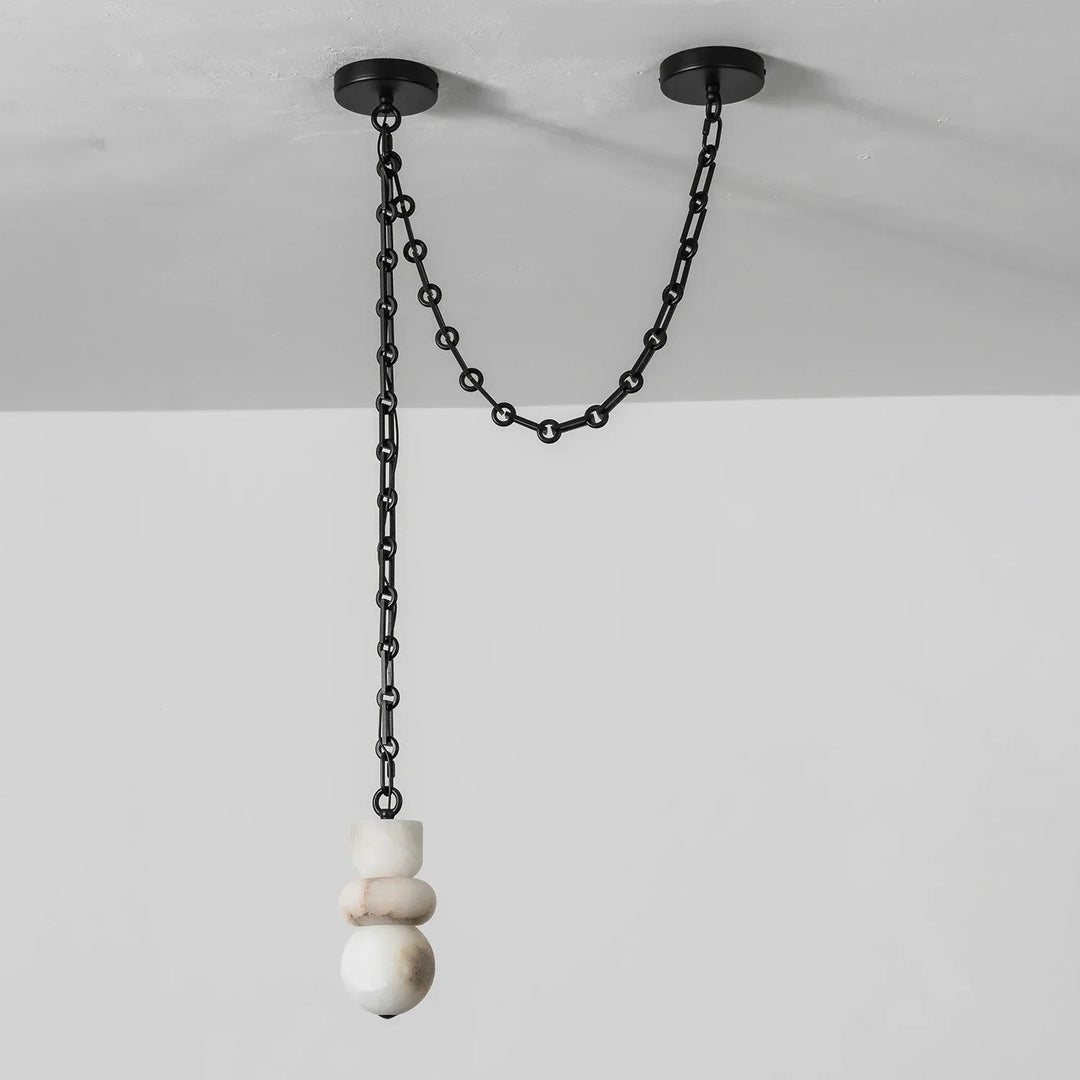 Unlit white alabaster chandelier hangs beneath a black chain looped between two ceiling mounts against a pale wall.