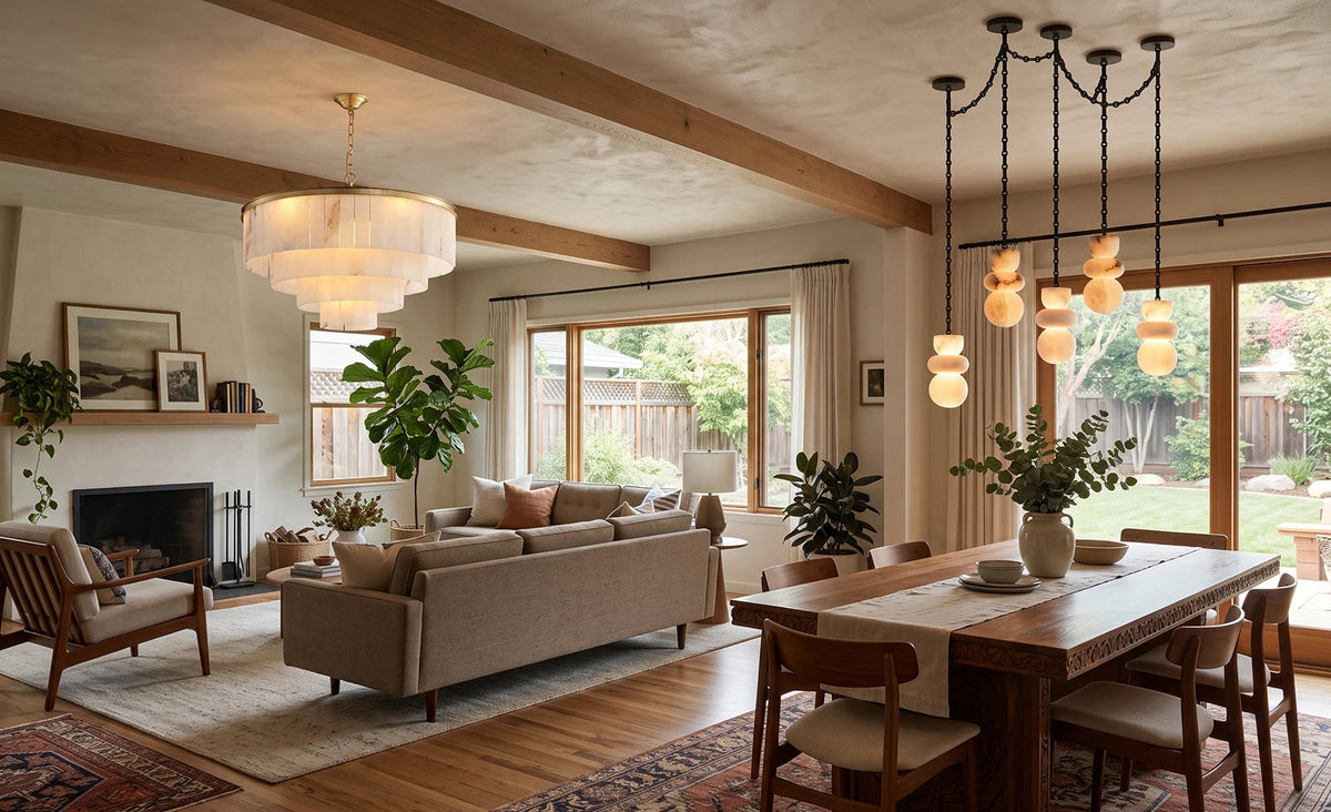 A modern, warm-toned living room and dining area featuring a large tiered white chandelier, a multi-light cluster pendant, a beige sofa, a wooden dining table, and large windows looking out to a backyard.