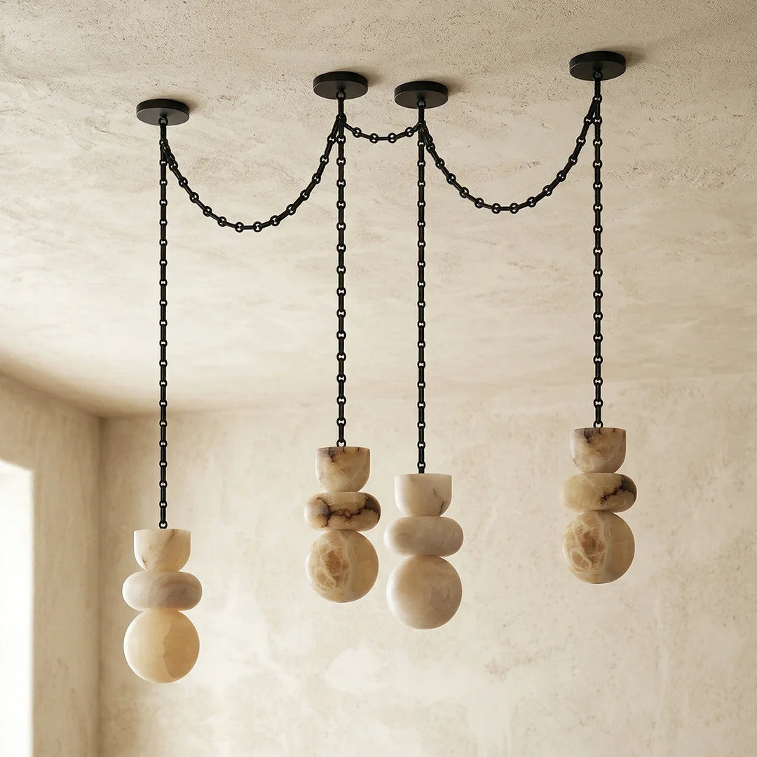 Unlit alabaster chandelier with four veined cream stone drops and draped black chains against pale textured walls.