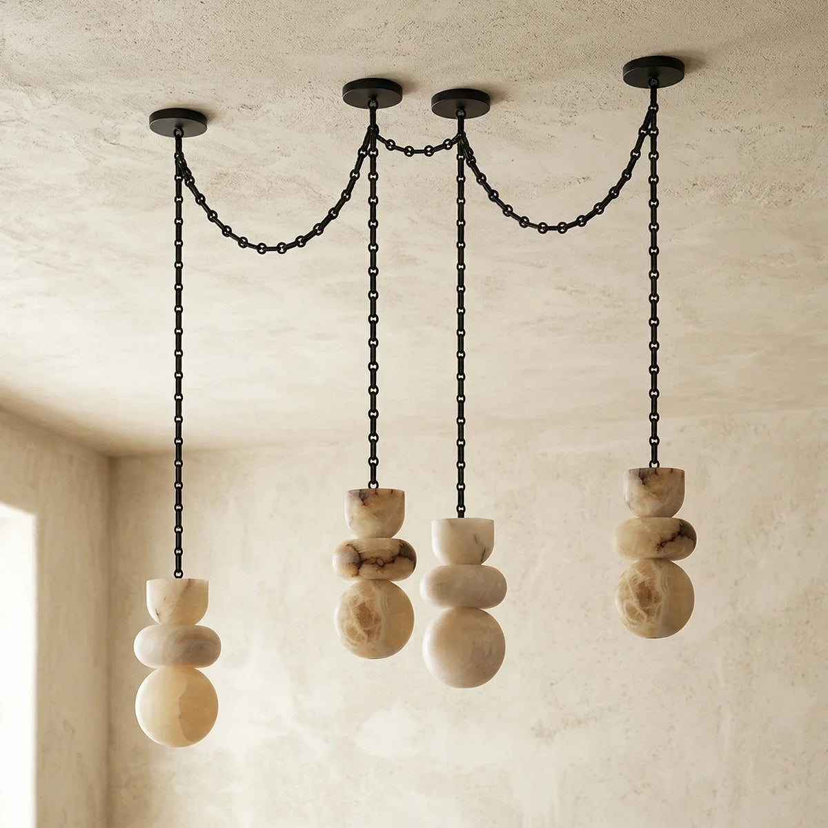 Unlit alabaster chandelier with four veined cream stone drops and draped black chains against pale textured walls.