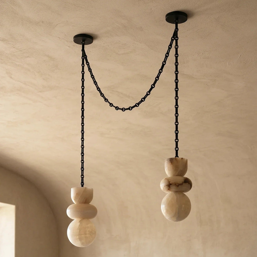 Unlit alabaster chandelier with two cream stone drops and draped black chains beneath a textured beige ceiling.