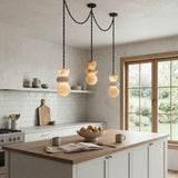 An alabaster chandelier with three stacked cream stone drops hangs above a wooden kitchen island beside large windows.