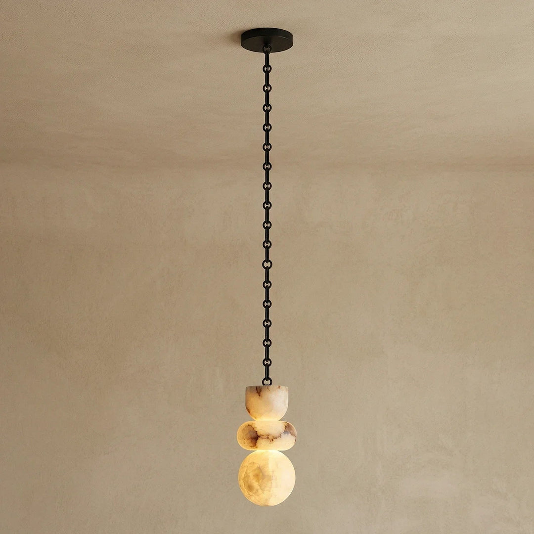 Single-light chandelier with a glowing, three-part alabaster shade showing cream and brown veining, suspended from a black chain against a beige wall.