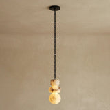 Single-light chandelier with a glowing, three-part alabaster shade showing cream and brown veining, suspended from a black chain against a beige wall.