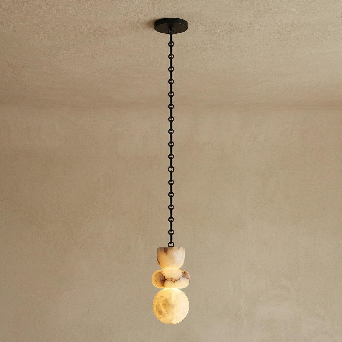Single-light chandelier with a glowing, three-part alabaster shade showing cream and brown veining, suspended from a black chain against a beige wall.