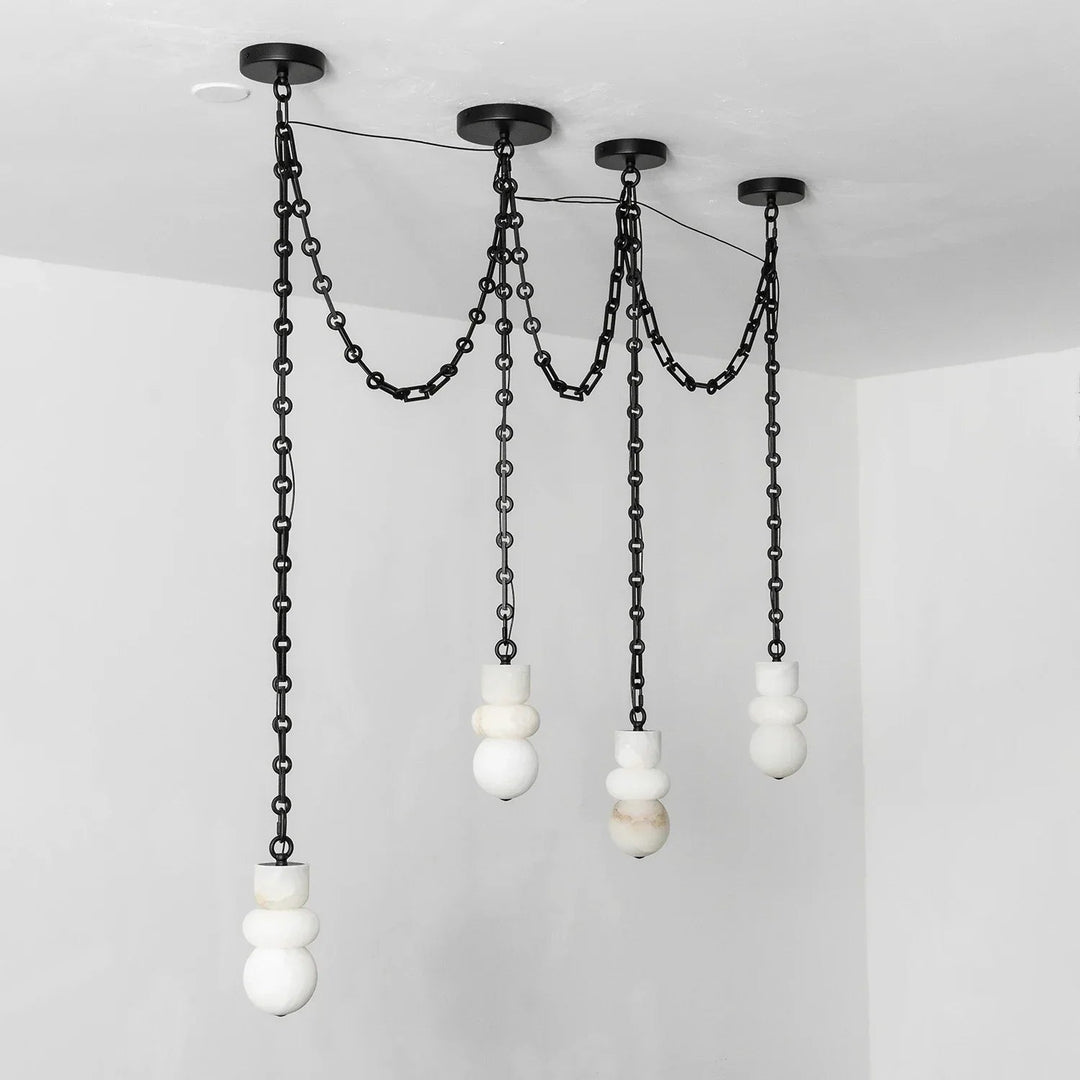 A modern multi-light pendant chandelier with matte black metal chains and spherical white and marble glass shades, suspended from a black ceiling canopy in a minimalist room.