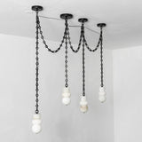 A modern multi-light pendant chandelier with matte black metal chains and spherical white and marble glass shades, suspended from a black ceiling canopy in a minimalist room.