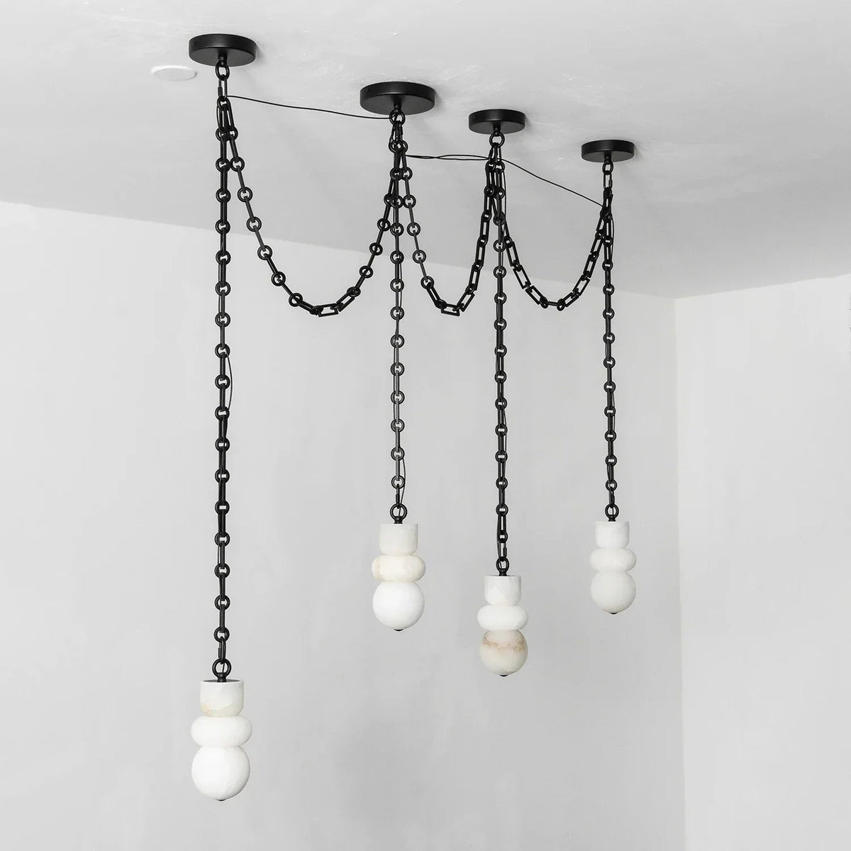 A modern multi-light pendant chandelier with matte black metal chains and spherical white and marble glass shades, suspended from a black ceiling canopy in a minimalist room.