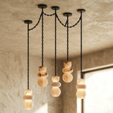 Alabaster chandelier with five illuminated cream stone drops suspended from black chains beside a window in a textured beige room.