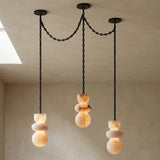 Alabaster chandelier with three illuminated cream stone drops hanging from connected black chains beside a ceiling opening.