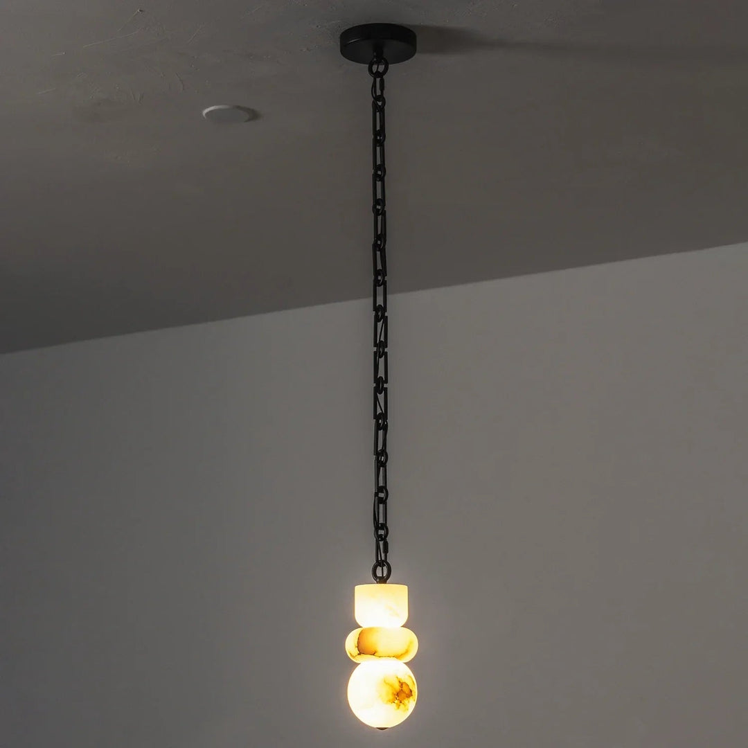 Alabaster chandelier glows warm yellow beneath a long black chain against a gray wall.