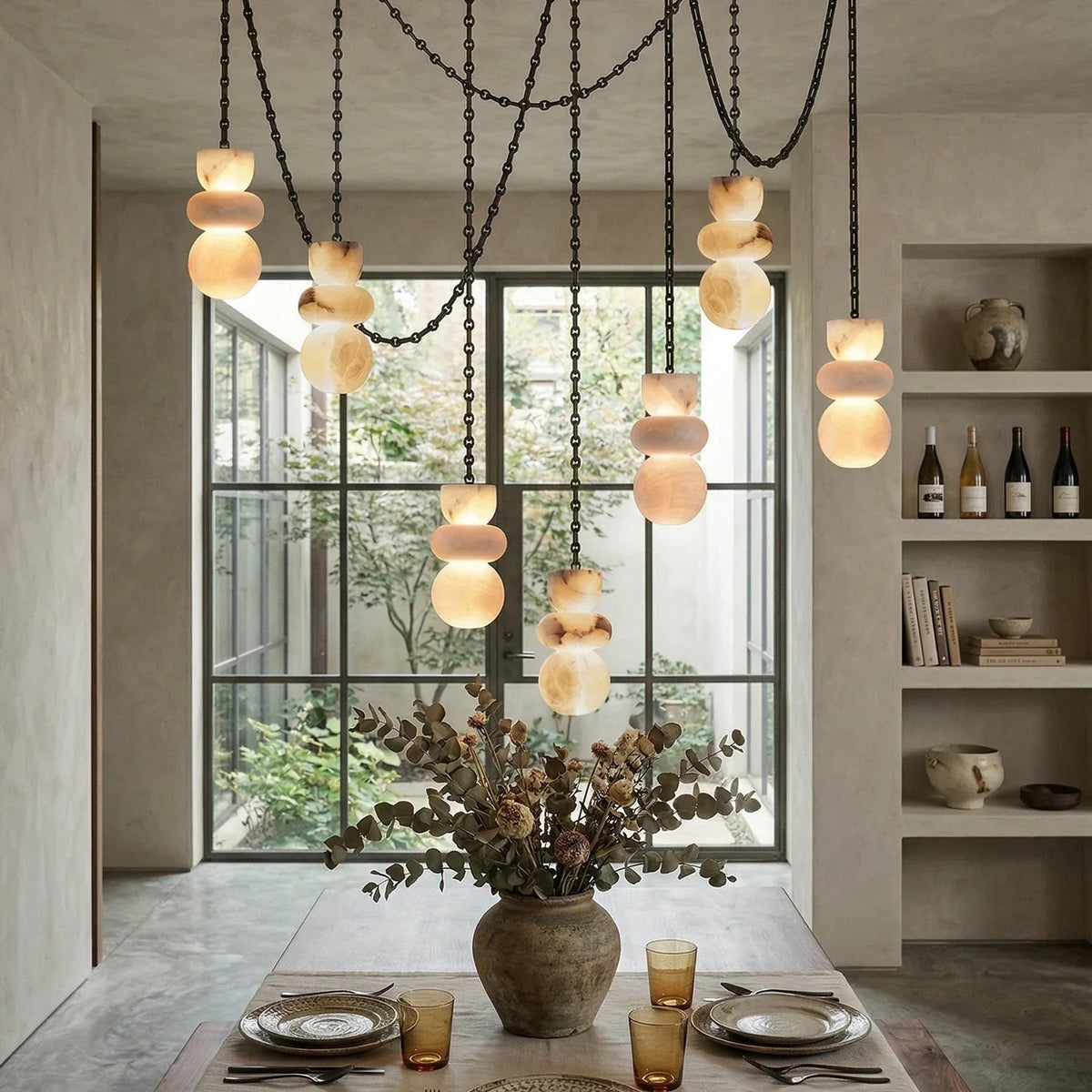 An alabaster chandelier with seven glowing cream stone drops hangs at staggered heights above a dining table with a large floral arrangement.