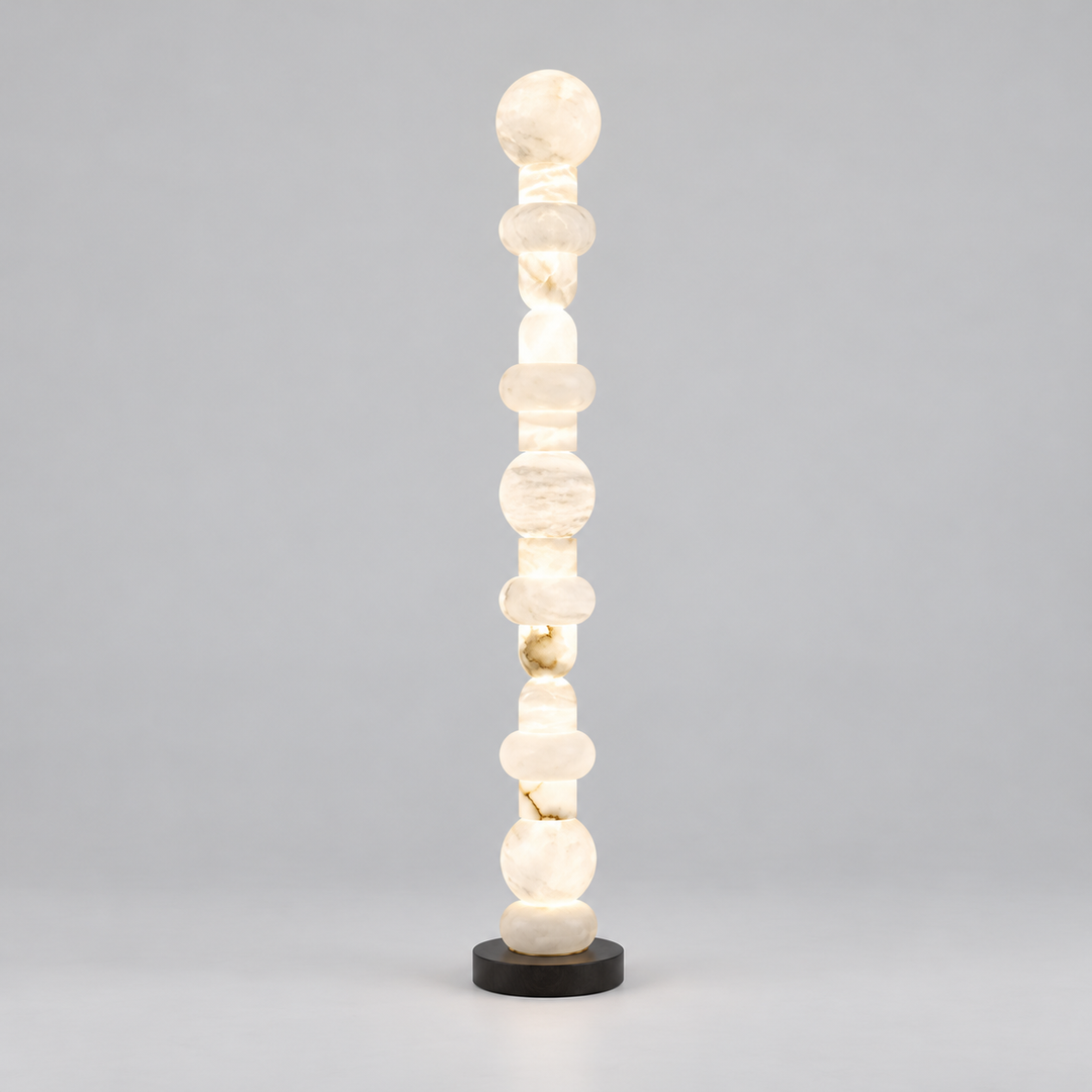 A modern chakra-style floor lamp made of stacked translucent white stone beads on a round black base, photographed against a neutral gray studio background.