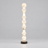 A modern chakra-style floor lamp made of stacked translucent white stone beads on a round black base, photographed against a neutral gray studio background.