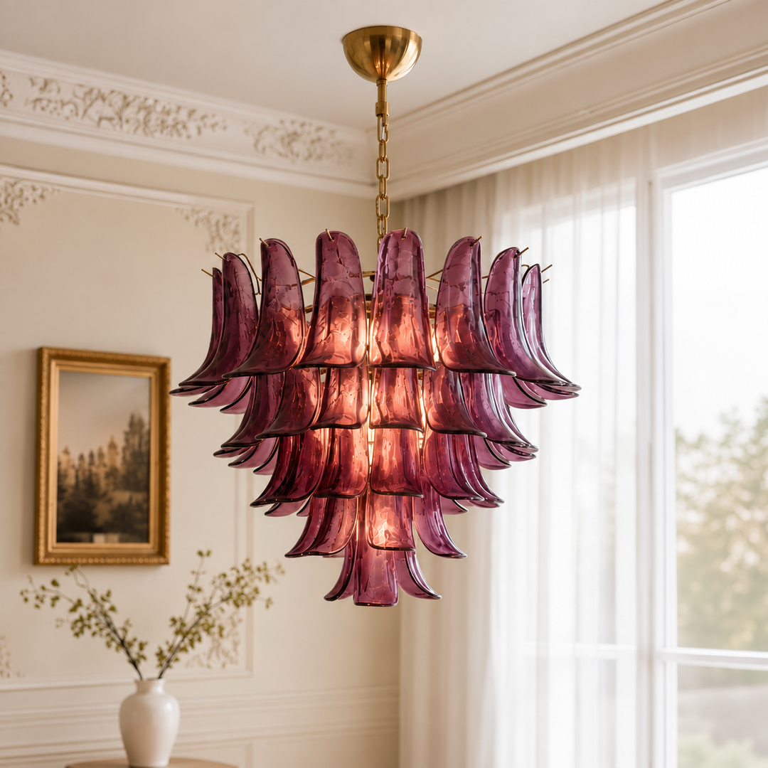 A mid-century modern tiered chandelier made of textured, translucent burgundy glass petal-like shades, suspended from a gold brass chain and canopy in a classic cream-colored room.